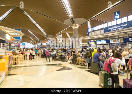 Reisende, die durch die Gegend gehen und ihre Abfertigungsschalter am identifizieren Hauptabflugshalle des Flughafens KLIA Stockfoto