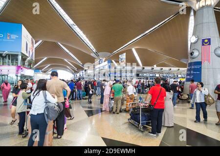 Reisende, die durch die Gegend gehen und ihre Abfertigungsschalter am identifizieren Hauptabflugshalle des Flughafens KLIA Stockfoto