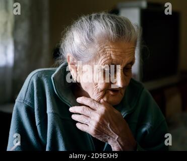 Alte depressive Frau. Eine ältere einsame Frau sitzt an einem Tisch in der Küche neben dem Fenster Stockfoto