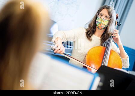 Hannover, Deutschland. November 2020. Musikpädagogin Sophia Grest spielt ihr Cello während eines Unterrichts an der städtischen Musikschule, mit einem Mund-und-Nase-Cover. Die mehr als 70 öffentlichen und gemeinnützigen Musikschulen Niedersachsens können aufgrund ihrer Einstufung als Bildungseinrichtungen trotz der teilweisen Sperrung im November weiterhin geöffnet bleiben. Beim Musizieren müssen Lehrer und Schüler eine Mundschutz tragen. Quelle: Hauke-Christian Dittrich/dpa/Alamy Live News Stockfoto