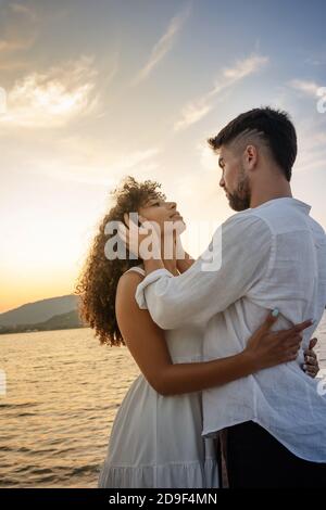 Junge attraktive kaukasischen bärtigen Mann mit modernen Haarschnitt hält seine Der Kopf der schwarzen hispanischen Freundin in den Händen und schaute in sie hinein Augen, während sie umarmt Stockfoto