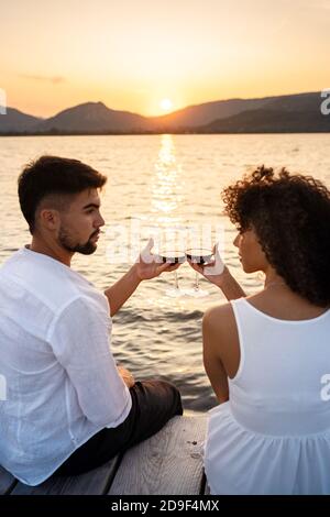 Romantikszene des multirassischen Paares, das auf einem Pier sitzt Sonnenuntergang oder Morgenröte mit Rotwein, der sich gegenseitig sieht In den Augen - attraktive Mann Bindung Stockfoto