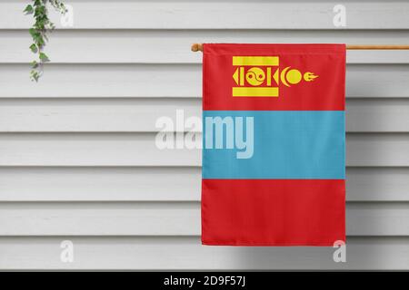 Die Nationalflagge der Mongolei hängt an einem Zaun entlang der Holzmauer in einer ländlichen Stadt. Konzept des Unabhängigkeitstages. Stockfoto