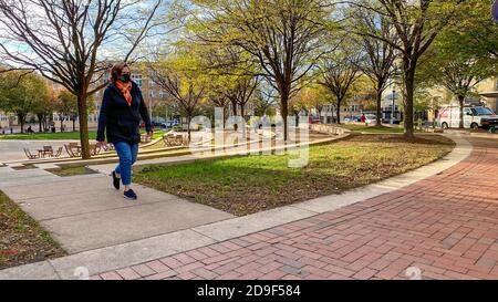 Reston, VA, USA – 3. November 2020. Ein Weitwinkelfoto einer Frau, die an einem Herbstnachmittag im Reston Town Center Park spazieren geht. Stockfoto