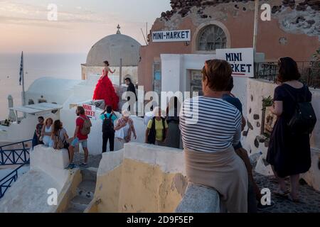 Eine orientalische Braut in ihrem leuchtend roten Kleid mit ihrem Bräutigam in Anwesenheit nimmt ihre Bilder auf einem Flachdach auf, während sich Touristen versammeln, um den berühmten Sonnenuntergang in der Stadt Oia auf der griechischen Ferieninsel Santorini zu beobachten. 19. Oktober 2015. Foto: Neil Turner Stockfoto