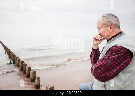 Nachdenklicher älterer Mann, der am Strand auf einem nebligen stand Tag Stockfoto