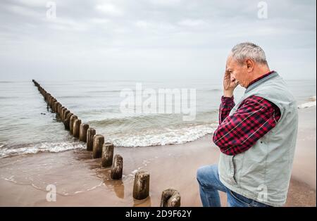 Nachdenklicher älterer Mann, der am Strand auf einem nebligen stand Tag Stockfoto