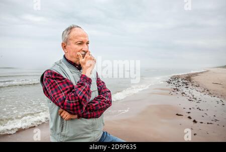 Nachdenklicher älterer Mann, der am Strand auf einem nebligen stand Tag Stockfoto