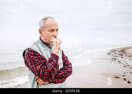 Nachdenklicher älterer Mann, der am Strand auf einem nebligen stand Tag Stockfoto