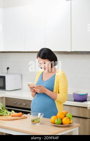 Glückliche schwangere Frau mit Sprachbefehl Recorder auf dem Smartphone Stockfoto