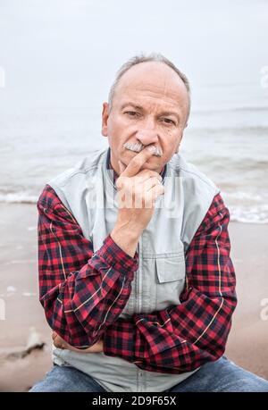 Nachdenklicher älterer Mann am Strand an einem nebligen Tag Stockfoto