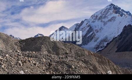 Menschen wandern durch den felsenbedeckten majestätischen Khumbu-Gletscher auf dem Weg zum Dorf Gorakshep auf dem Everest Base Camp Trek mit schneebedecktem Nuptse. Stockfoto