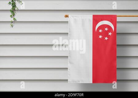 Singapur nationale kleine Flagge hängt von einem Pfostenzaun entlang der Holzmauer in einer ländlichen Stadt. Konzept des Unabhängigkeitstages. Stockfoto