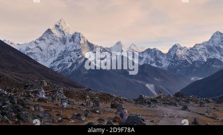 Denkmal für die toten Bergsteiger in der Nähe von Lobuche, Himalaya, Nepal mit Steinmonumenten, bunten buddhistischen Gebetsfahnen und majestätischen Himalaya-Bergen. Stockfoto