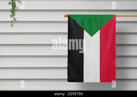 Sudanesische Nationalflagge hängt an einem Zaun entlang der Holzmauer in einer ländlichen Stadt. Konzept des Unabhängigkeitstages. Stockfoto