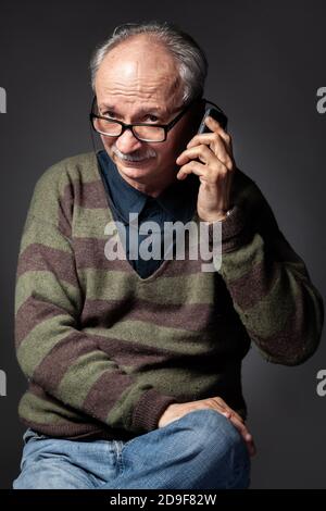 Studioportrait eines älteren müden Mannes auf dunklem Hintergrund. Sprechen auf einem Handy Stockfoto