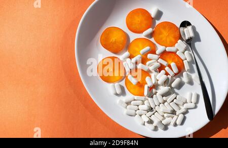 Orangefarbene runde Scheiben von weißen Pessimmon-Tabletten und einem Metalllöffel mit Pillen auf einer weißen Teekanne. Nahrungsergänzungsmittel und gesunde Ernährung. Stockfoto