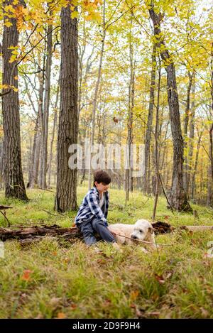 Kleiner Junge, der an einem Herbsttag mit seinem Hund im Wald spielt. Stockfoto