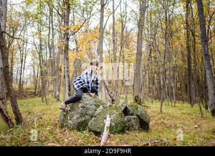 Kleiner Junge, der an einem Herbsttag auf einem großen Felsen im Wald klettert. Stockfoto