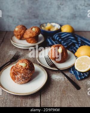 Mit Zitronen gefüllte Cruffins auf Holztisch mit Tellern und Gabeln. Stockfoto