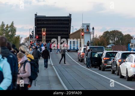 Zingst, Deutschland. Oktober 2020. Dutzende Touristen stehen auf der Meinigbrücke, um Kraniche zu beobachten. (l) auf der anderen Straßenseite (r) warten Autofahrer darauf, dass die erhöhte Liftbrücke wieder für den Verkehr geöffnet wird. Die Meininger Brücke verbindet das Festland mit der Halbinsel Fischland-Darß-Zingst. Die Brücke war Teil einer Eisenbahnlinie von 1910. In der Zwischenzeit ist ein Neubau für die Eisenbahn, Autos, Radfahrer und Fußgänger geplant. Quelle: Stephan Schulz/dpa-Zentralbild/ZB/dpa/Alamy Live News Stockfoto