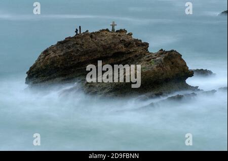 La Roche Battue (der zerschlagene oder geschlagene Felsen), der bei Flut nicht weit in die stürmische Bucht von Biscay vor dem Grand Plage Strand in Biarritz, Nouvelle-Aquitaine, Frankreich, liegt. Sie trägt ein beschriftete Kreuz und andere Gedenkstätten an die ertrunkene fünfköpfige Besatzung der Schlinge ‘La Surprise’, die in rauschenden Meeren Segel und Ruder verlor, während sie Schiefer von Bayonne nach London, England, transportete. Das Schiff lief am nächsten Tag, dem 17. November 1893, auf La Roche Battue, auch bekannt als l’Arroque Trudade, auf Grund. Ein Mann wurde tot aufgefunden, aber die Leichen der anderen vier wurden nie geborgen. Stockfoto