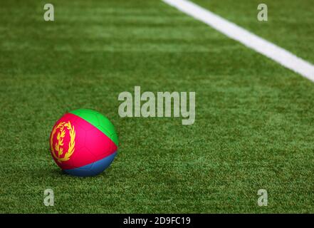 Eritrea Flagge auf Ball im Fußballfeld Hintergrund. Fußball-Nationalthema auf grünem Gras. Konzept des Sportwettbewerbs. Stockfoto