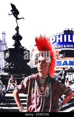 London Punk Rocker Matt Belgrano posiert neben der Statue von Eros, Piccadilly Circus, London, England, UK. Ca. 1980 Stockfoto