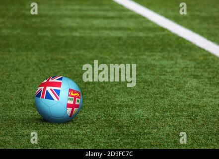 Fidschi-Flagge auf Ball im Fußballfeld Hintergrund. Fußball-Nationalthema auf grünem Gras. Konzept des Sportwettbewerbs. Stockfoto
