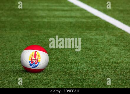 Französisch-Polynesien Flagge auf Ball auf Fußballplatz Hintergrund. Fußball-Nationalthema auf grünem Gras. Konzept des Sportwettbewerbs. Stockfoto