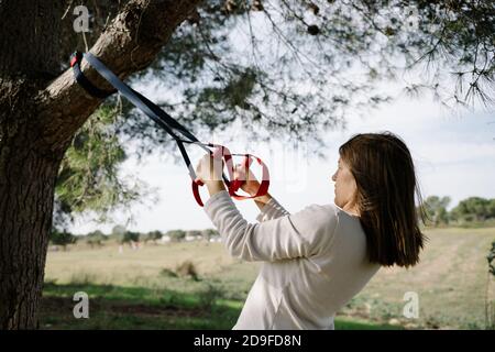TRX Sport Team. Junge Frau macht Übungen im Freien in einem Park. Riemen Stockfoto