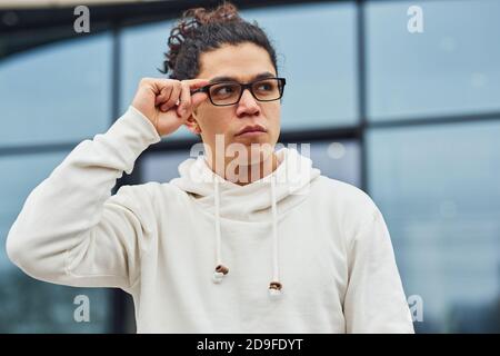 Schöner junger Mann mit lockigen schwarzen Haaren ist auf der Straße gegen Gebäude Stockfoto