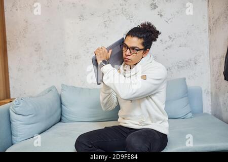 Wütend junger Mann mit lockigen schwarzen Haaren geht verrückt und Wütend auf Laptop in den Händen Stockfoto