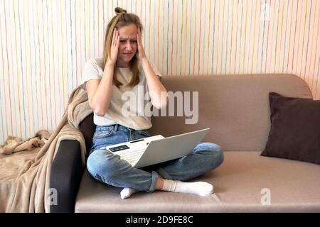 Junge frustrierte Frau, die während der Quarantäne von zu Hause aus arbeitet covid-19 vor dem Laptop, der unter chronischen täglichen Kopfschmerzen leidet. Freiberufliche Tätigkeit Stockfoto