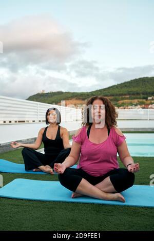 Zwei Frauen üben Yoga auf der Terrasse des Hauses, Lotushaltung Stockfoto