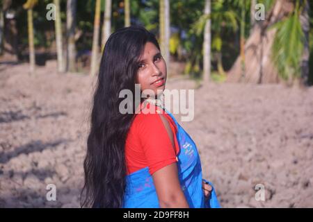 Nahaufnahme Seite Gesicht eines indischen Teenager-Mädchen trägt blauen Sari mit roter Bluse Nase Pin großen Ohrring auf einem gepflügten Feld, selektive Fokussierung Stockfoto