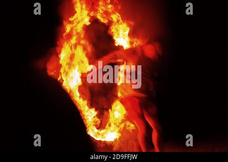 Vor dem Hintergrund der menschlichen Silhouette fällt eine andere verschwommene Person aus dem Feuersturm. Unkenntlich verschwommene anonyme Silhouette in der Nacht Stockfoto