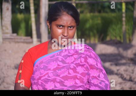 Nahaufnahme eines Teenagers in Bengali, das Sari mit langen Haaren und goldener Nasennadel trägt, Ohrringe in einem gepflügten Feld, selektive Fokussierung Stockfoto