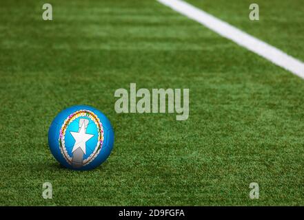 Nördliche Marianen Flagge auf Ball auf Fußballplatz Hintergrund. Fußball-Nationalthema auf grünem Gras. Konzept des Sportwettbewerbs. Stockfoto