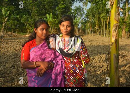 Nahaufnahme von zwei schönen indischen Bengali Teenage Mädchen tragen Rosa Sari und Salwar Kameez mit Ohrringen Nase Pin posiert In einem gepflügten landwirtschaftlichen Fie Stockfoto