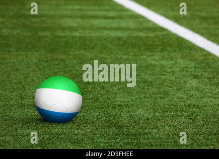 Sierra Leone Flagge auf Ball auf Fußballplatz Hintergrund. Fußball-Nationalthema auf grünem Gras. Konzept des Sportwettbewerbs. Stockfoto