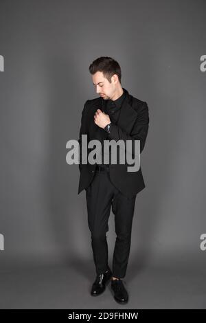 Studioportrait eines jungen kaukasischen Mannes in einem schwarzen Blazer, der nach unten schaut, Hand auf Brust, vor schlichtem Studiohintergrund stehend Stockfoto