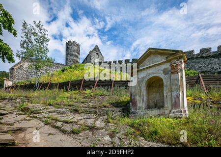 Bezdez, Tschechische Republik - Juli 19 2020: Blick auf die Kapelle, den Turm und ein Haus, Teile der mittelalterlichen Burg aus grauen Steinen auf einem grünen Hügel. Stockfoto