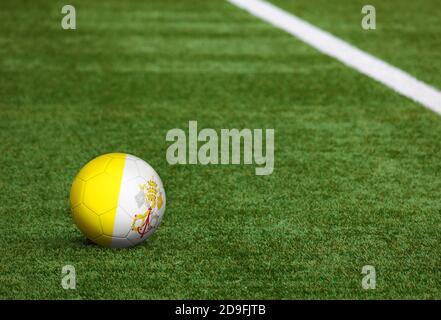 Vatikanstadt Flagge auf Ball auf Fußballplatz Hintergrund. Fußball-Nationalthema auf grünem Gras. Konzept des Sportwettbewerbs. Stockfoto