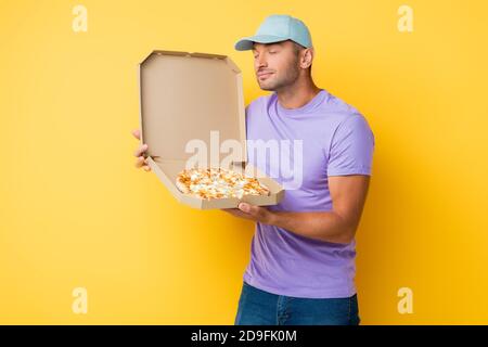Zufrieden Mann in blauer Kappe riecht leckere Pizza in Karton Feld auf gelb Stockfoto