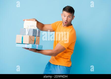 Überrascht Mann in T-Shirt hält verpackt Geschenke auf blau Stockfoto