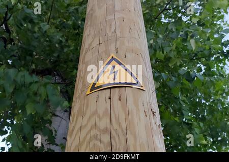 Zeichen der Gefahr eines elektrischen Schlags auf einem Holzmast. Schwarzer Blitz gegen ein gelbes Dreieck. Stock Foto mit leerem Platz für Text und Design. Stockfoto