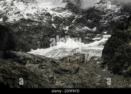 Im August, Monate vor dem Beginn des alpinen Winters, stürzt Schmelzwasser in den gestreift Felsen unter den Höhenschneefeldern und am Ende der Gletscher, die die zerklüfteten Hänge des Mont Blanc / Monte Bianco-Massivs hinunterschnappen, in Kanäle und Spalten. Aufnahme aus der Nähe von Entrèves, Courmayeur, Aostatal, Italien, in der Nähe des italienischen Eingangs zum 11.6 km (7.25 m) Mont-Blanc-Tunnel, der seit 1965 eine Alpenstraßenverbindung nach Frankreich bietet. Stockfoto