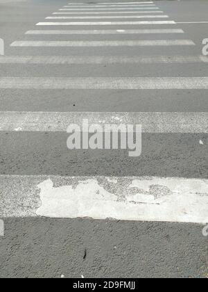 Fußgängerüberquerung durch die Straße. Weiße, schäbige, alte Streifen auf dem Asphalt. Das Konzept des Verkehrs, der städtischen Umwelt, des Straßenverkehrs und der Sicherheit. Stockfoto