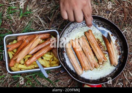 Bratkartoffeln und Hähnchenwürste im Freien anbraten Ein roter Mini-Gasherd und eine schwarze Bratpfanne Stockfoto